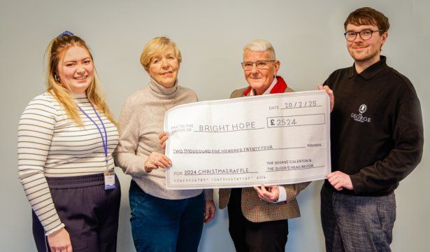 Four people holding an oversized check indoors, smiling at the camera.