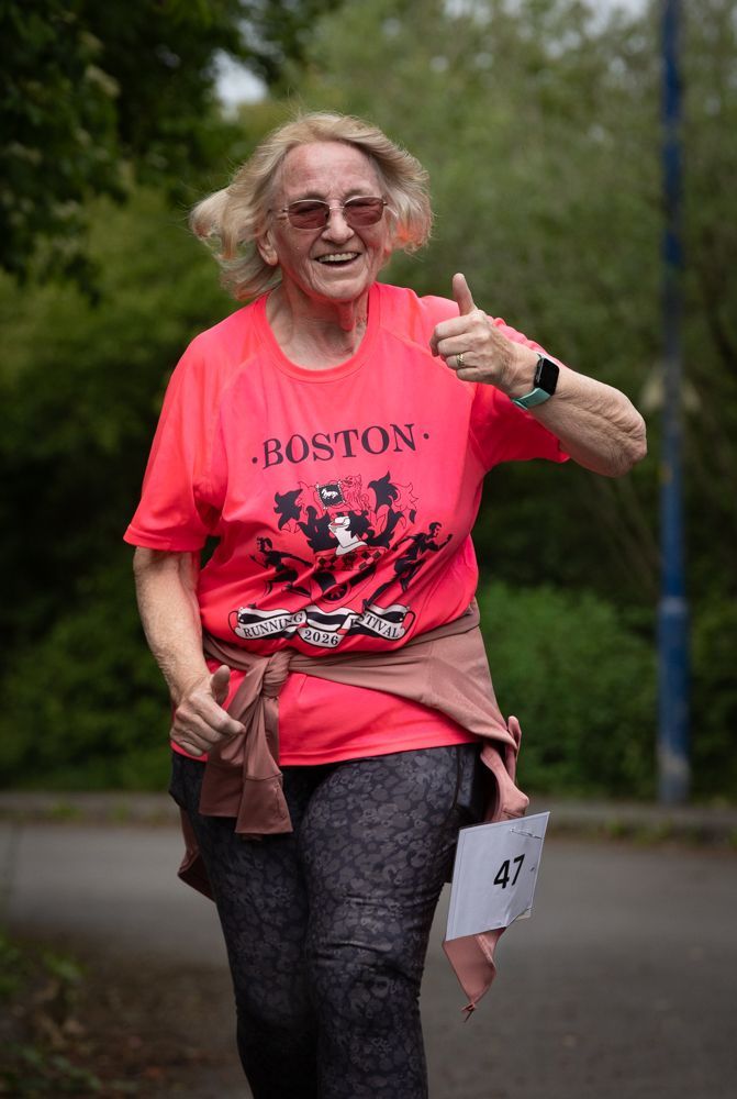 Runner in bright pink shirt giving a thumbs-up on a wooded road, wearing race bib 47.