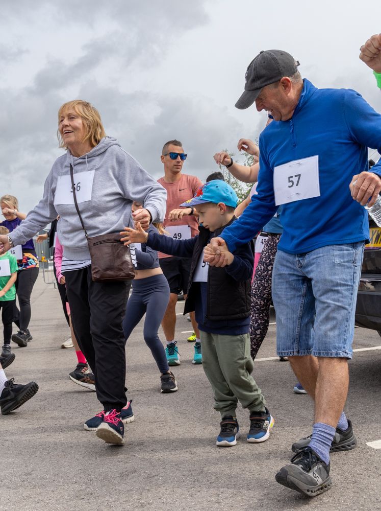 Runners in a race on a cloudy day, including a woman in gray, a child in a blue cap, and a man in blue.