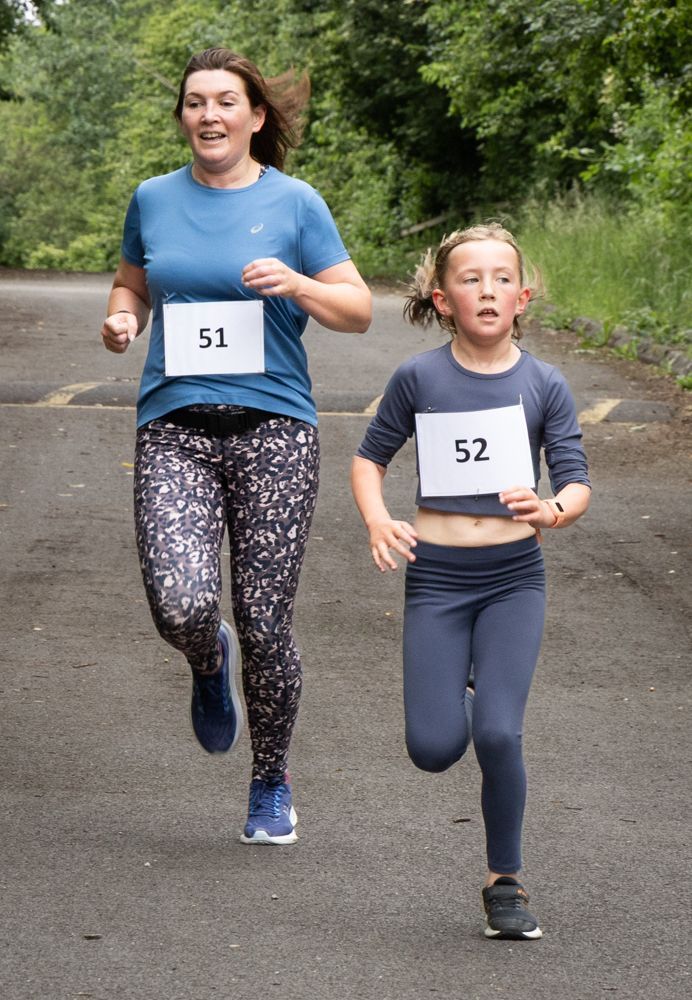 Two runners wearing bibs 51 and 52 jog on a tree-lined road
