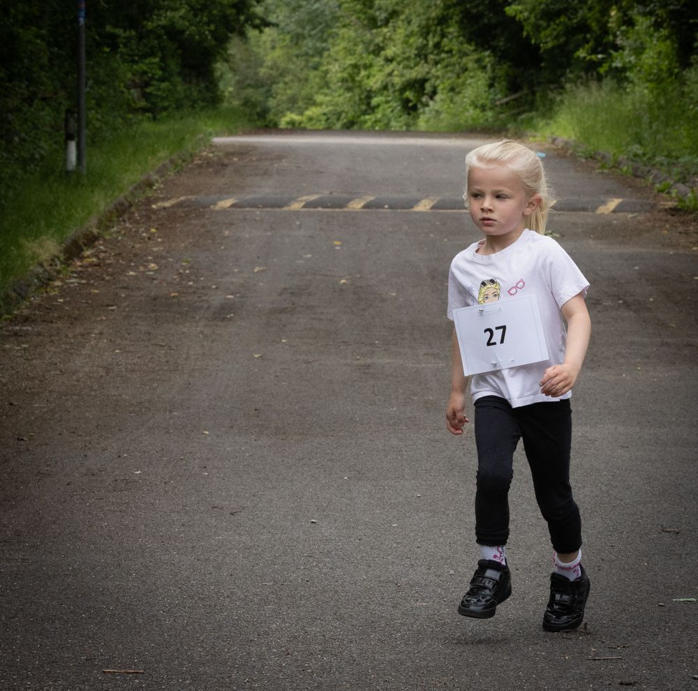Young child standing on a quiet road with trees, wearing a white shirt and black leggings