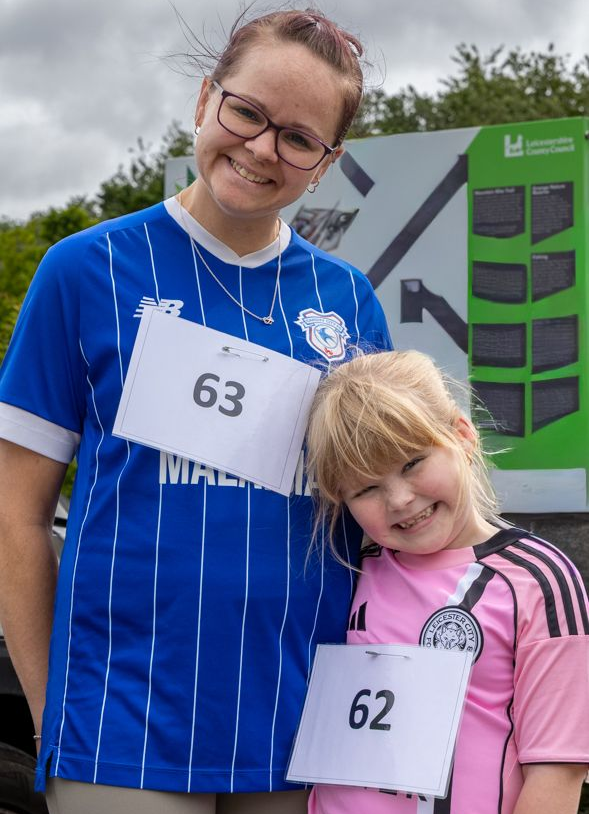 Two runners wearing bibs 63 and 62 pose together outdoors, smiling in front of a race backdrop.