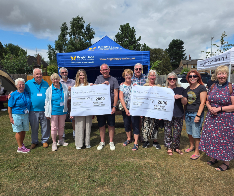 Group posing outdoors at charity event, holding oversized donation checks in front of a blue tent.