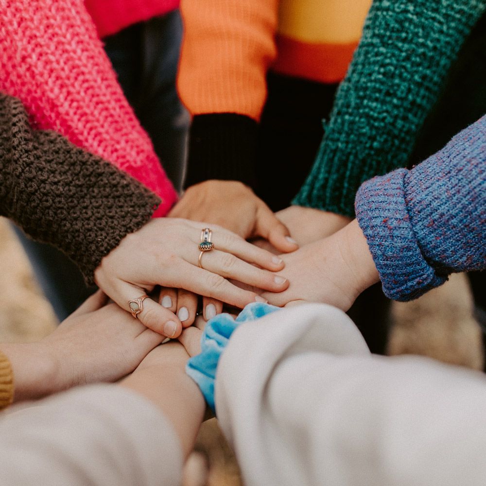 Hands stacked together in a circle, with colorful knit sleeves around them.