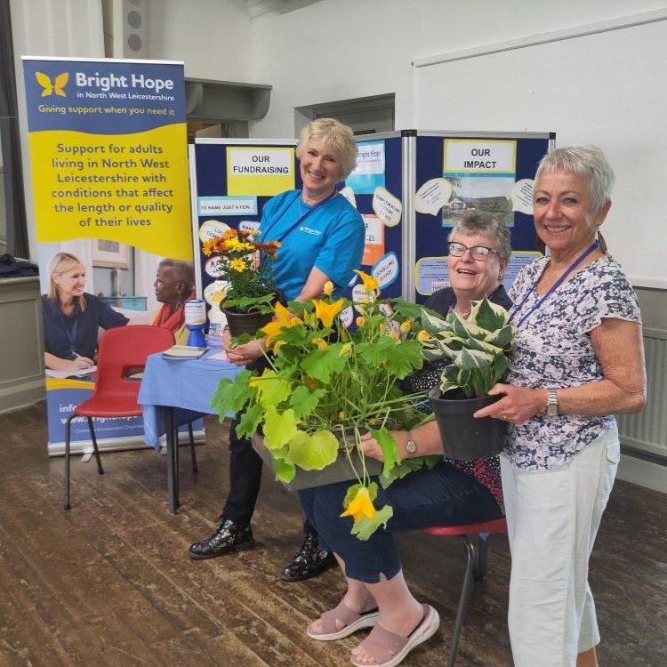 Three women with flowers at a Bright Hope community event booth indoors