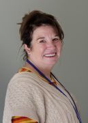 Smiling woman in a beige sweater with a purple lanyard against a plain gray background