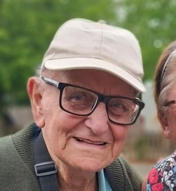 Smiling man in glasses and beige cap outdoors, with a green blurred background