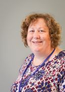 Smiling person in a patterned purple blouse against a plain gray background