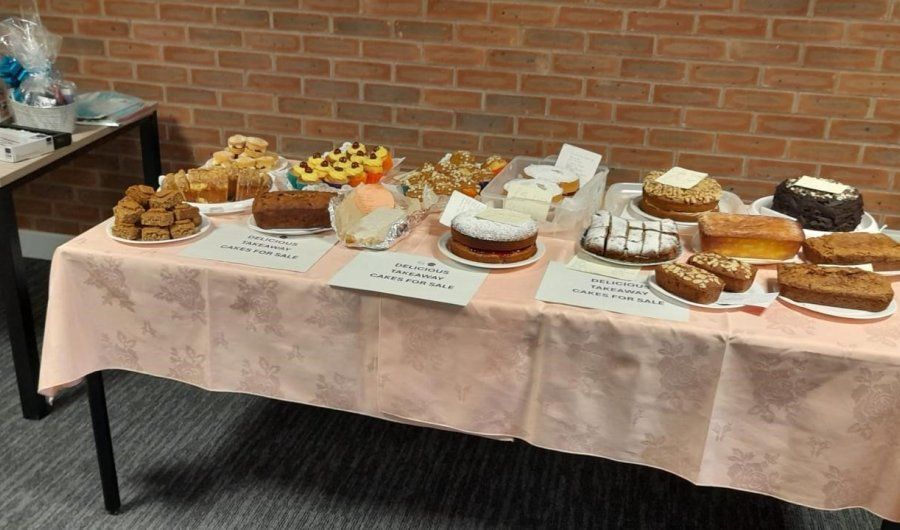 Dessert buffet on a table with cakes, pastries, fruit, and plates against a brick wall