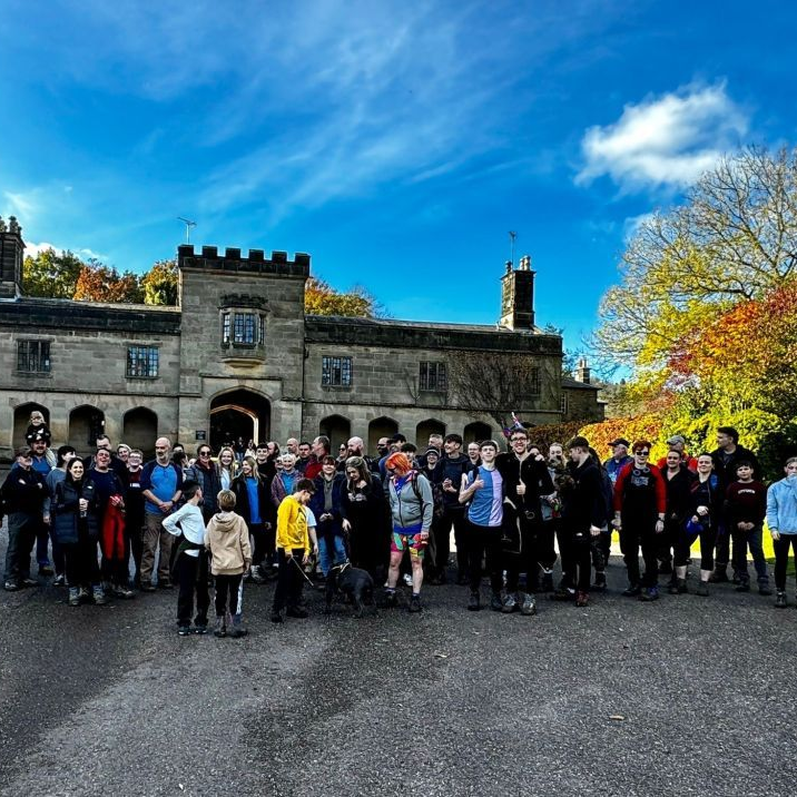 Large group gathered outside a stone castle under a bright blue sky, with autumn trees nearby