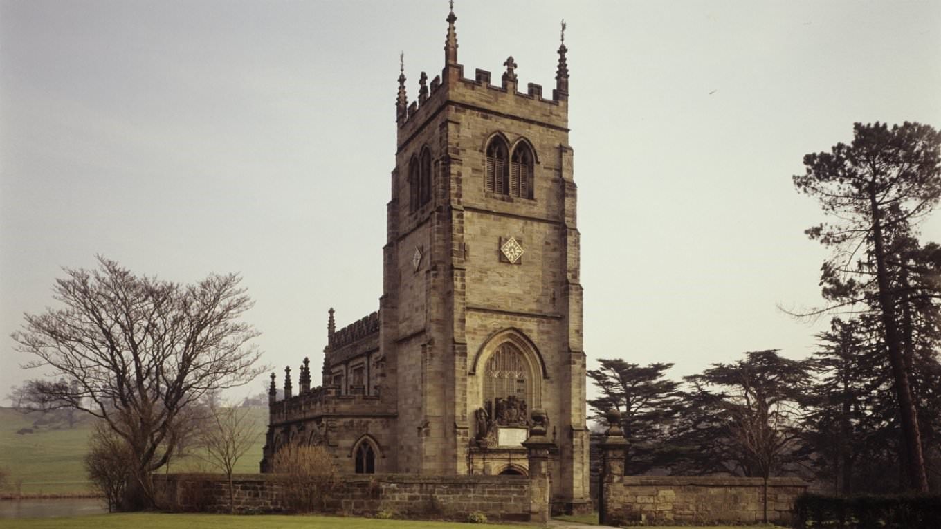 Stone church with tall square tower in a misty rural landscape, framed by bare trees.