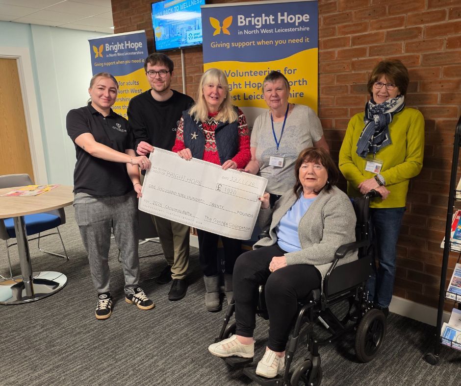 Group posing indoors with a large donation check in front of a Bright Hope banner