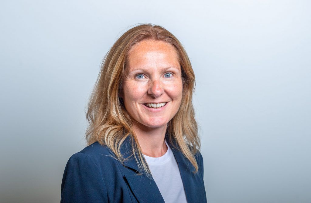 Smiling woman in a navy blazer and light blue shirt against a soft gray background