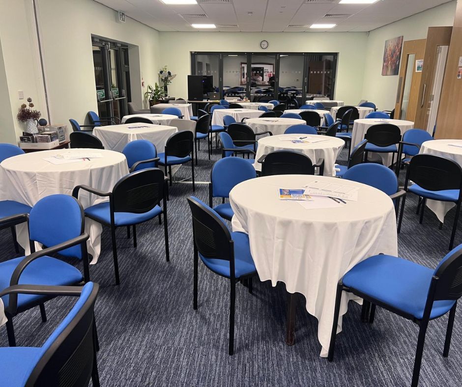 Empty meeting room with round tables draped in white and blue chairs arranged around them