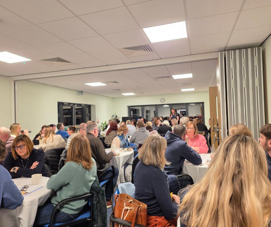 People seated at tables in a bright meeting room, listening and talking during a group event.