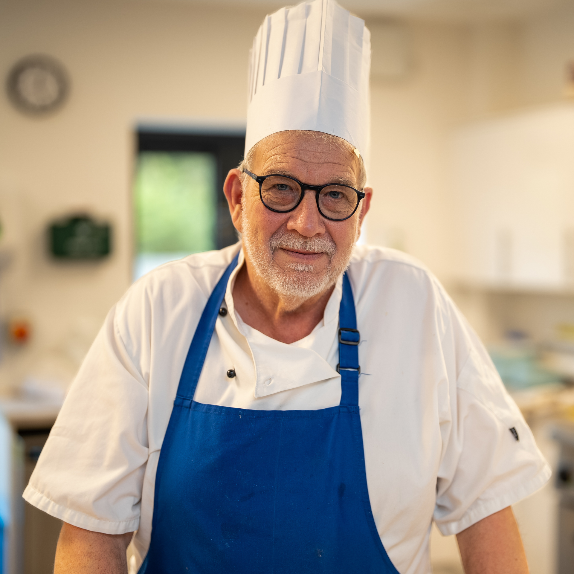 Chef in white uniform and blue apron smiling in a bright kitchen