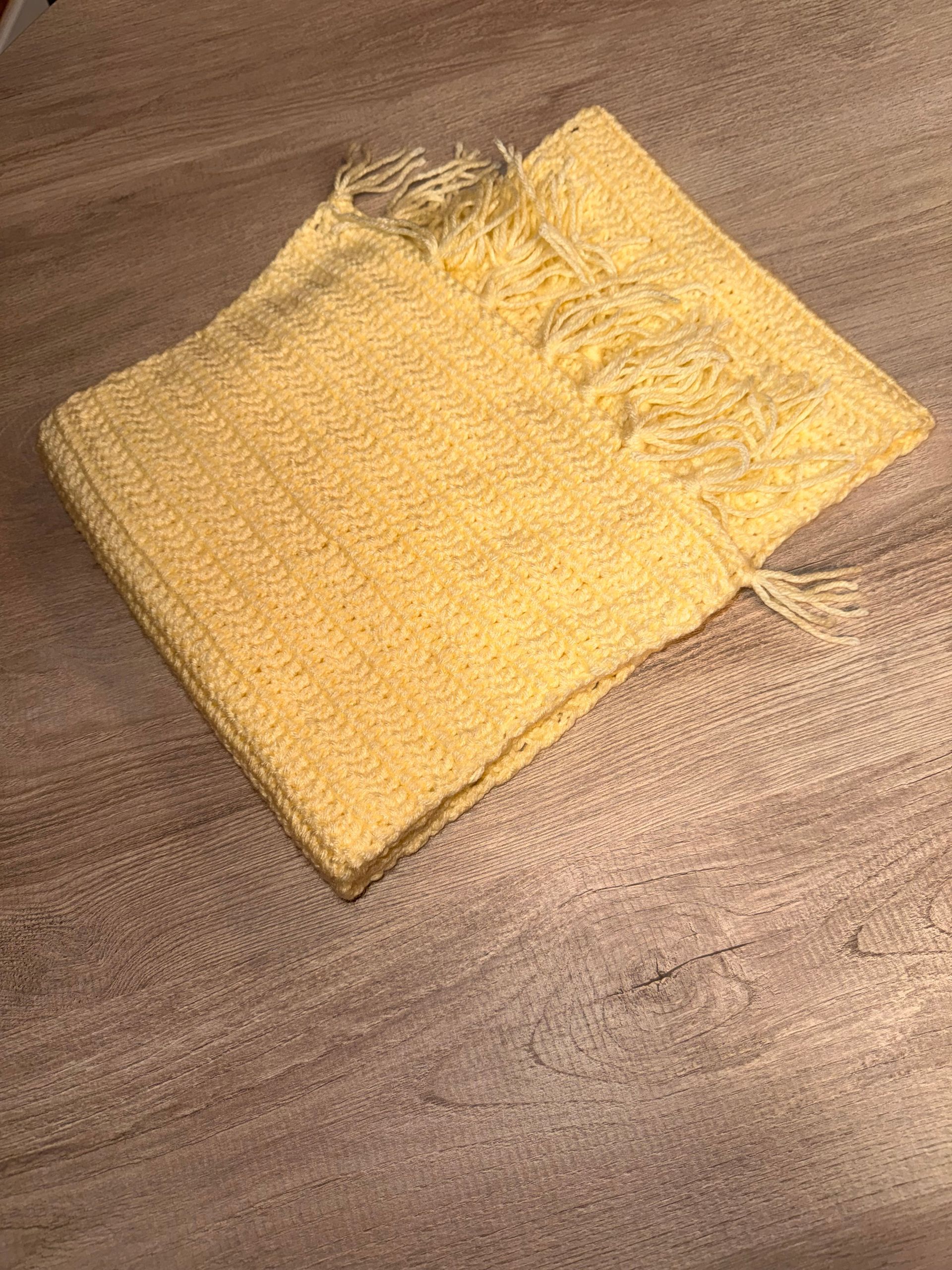 Yellow woven fabric square lying on a brown couch, with a frayed edge at the top.