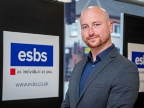 Man standing beside ESBS sign in an office, wearing a dark suit and smiling.