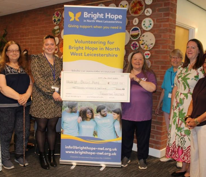 Bright Hope volunteers pose indoors with a large donation check and banner at a fundraising presentation.