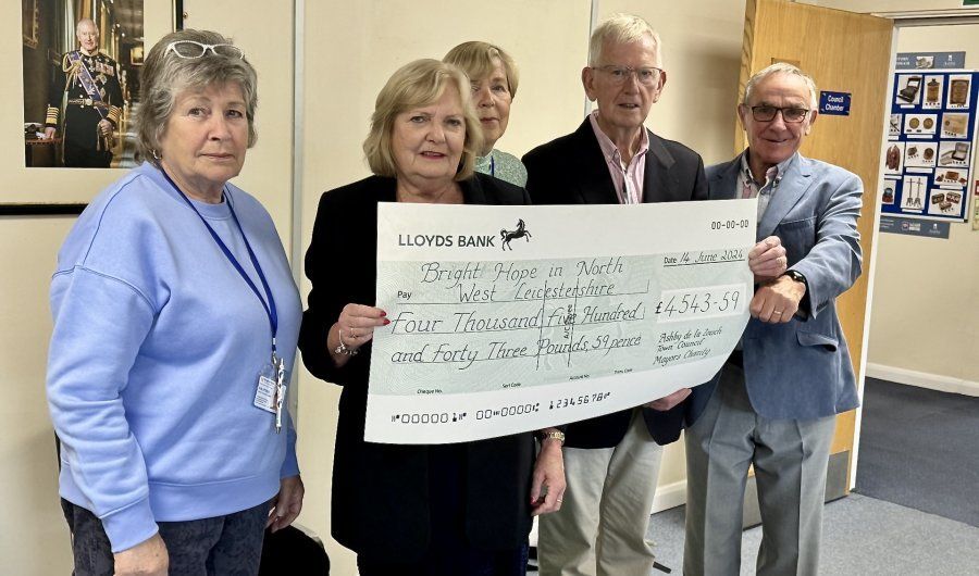 Four people holding a large check in a hallway, smiling at the camera.