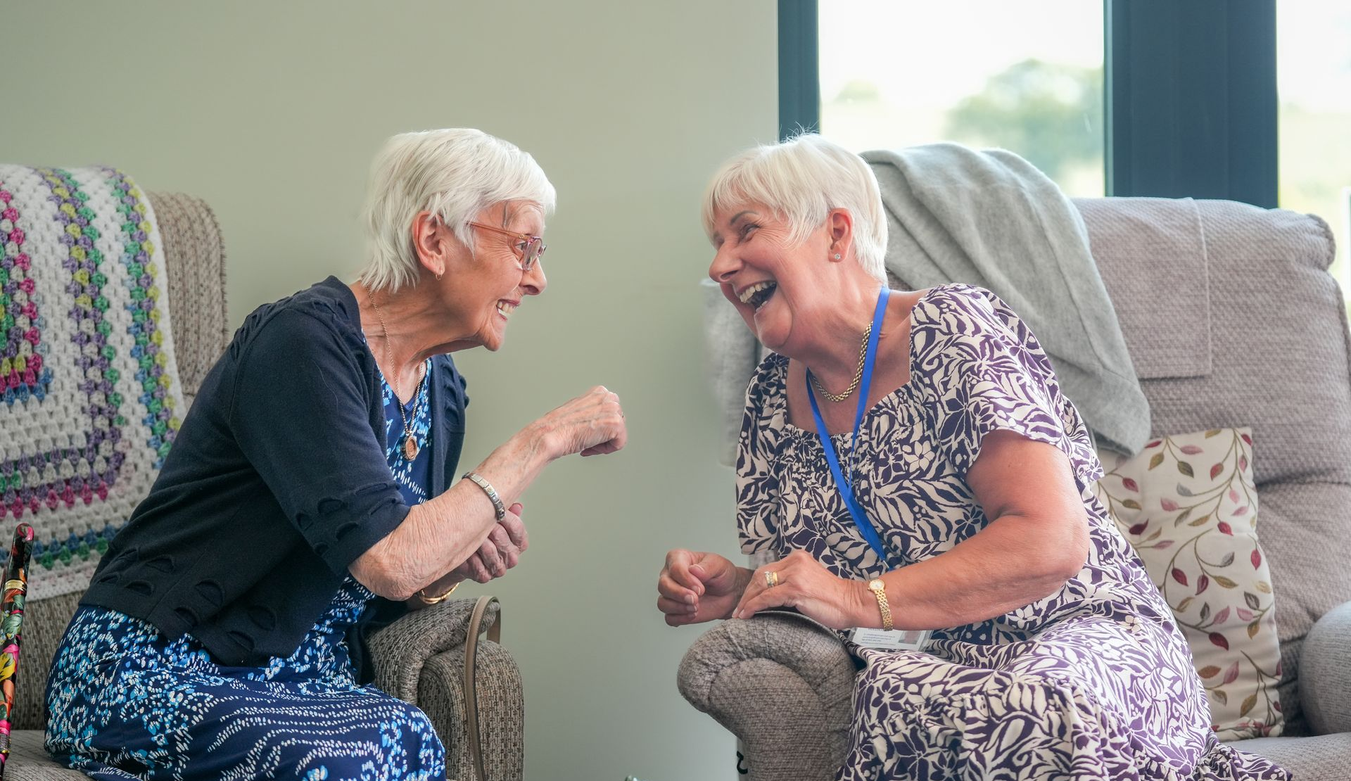 Two people laughing and talking on a couch in a bright living room