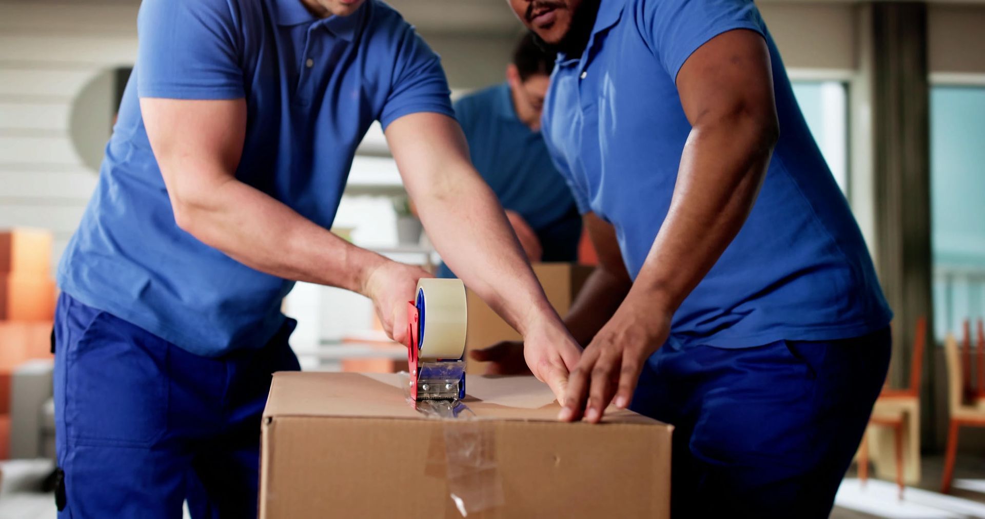 Two men are wrapping a cardboard box with tape.