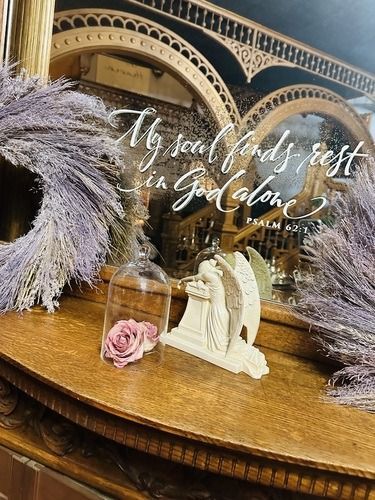 A decorative display with lavender wreath, angel statue, and a rose under glass, with a handwritten bible verse.