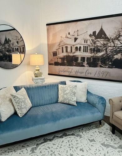 Blue velvet sofa with pillows, lamp, and framed historical house print.