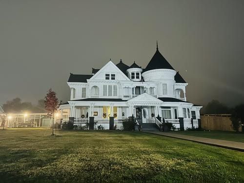 White Victorian house under a cloudy night sky, lit by soft light.