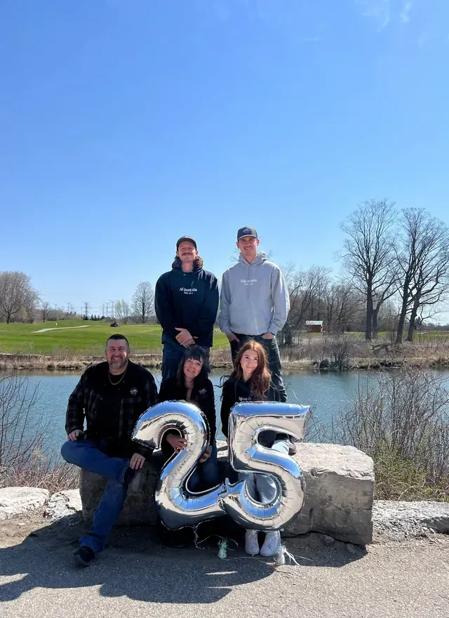 A group of people are posing for a picture with balloons in the shape of the number 25.