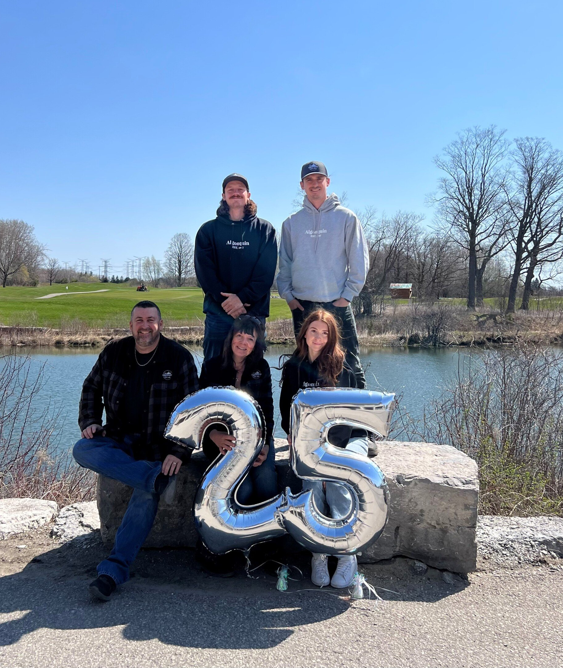 A group of people are posing for a picture with balloons in the shape of the number 25.