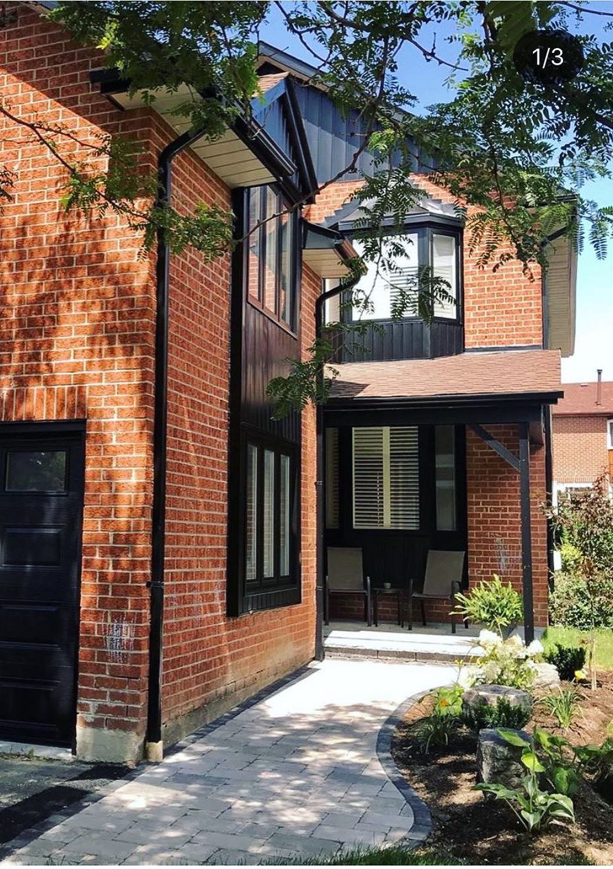 Brick house with black trim, garage door, and a covered porch with a slatted door. A stone pathway leads to the entrance.