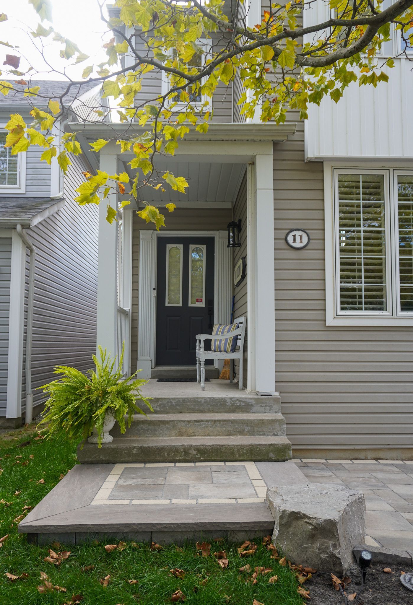 The front porch of a house with a black door and a white chair.
