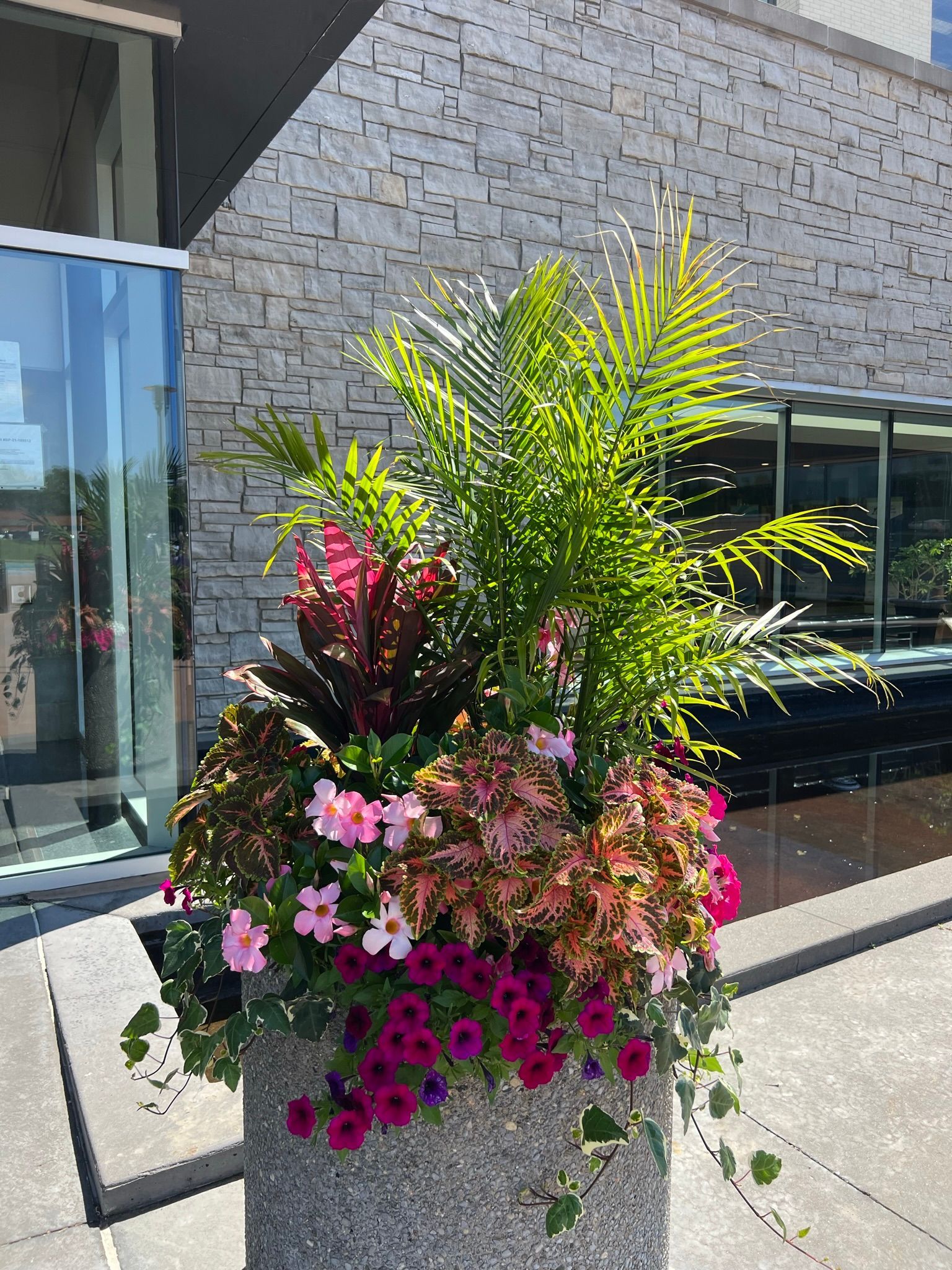 A planter filled with flowers and plants is sitting in front of a building.