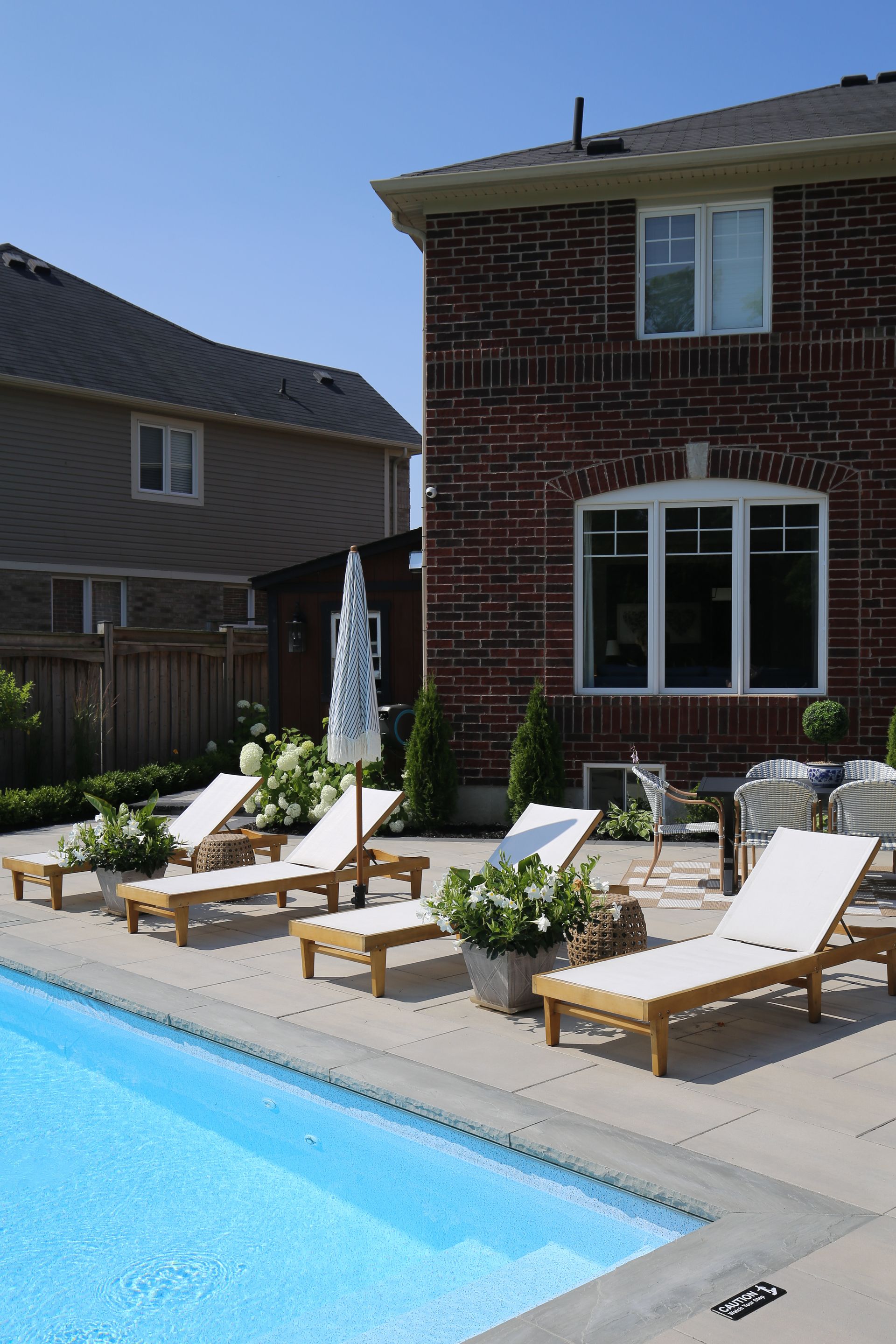 Poolside scene with lounge chairs, white flowers, and red brick house.