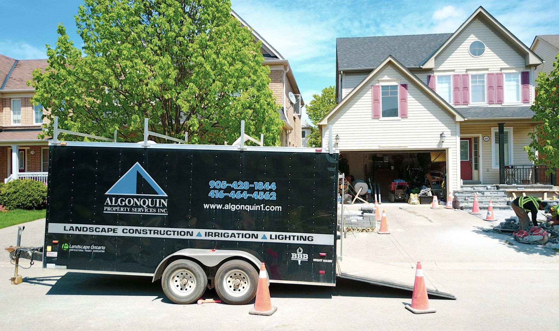 Black trailer with construction company logo parked in front of a house. Cones line the driveway.