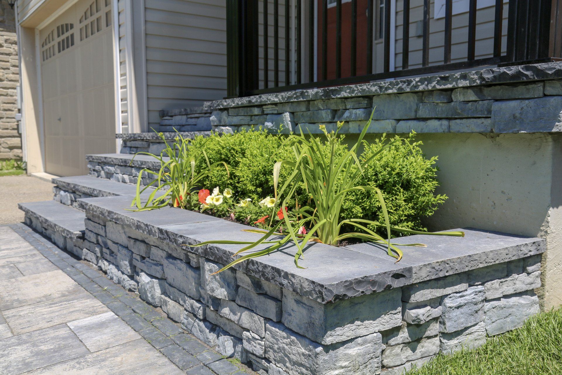 A stone wall with flowers growing on it in front of a house.