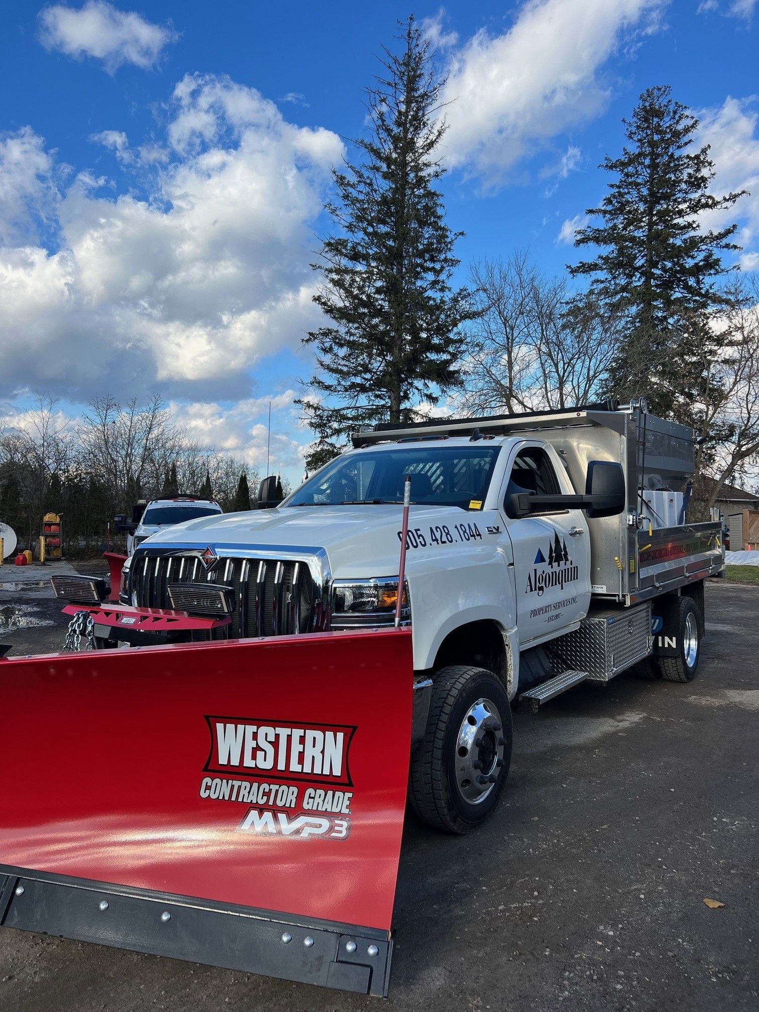 A white truck with a red snow plow on the back is parked in a parking lot.