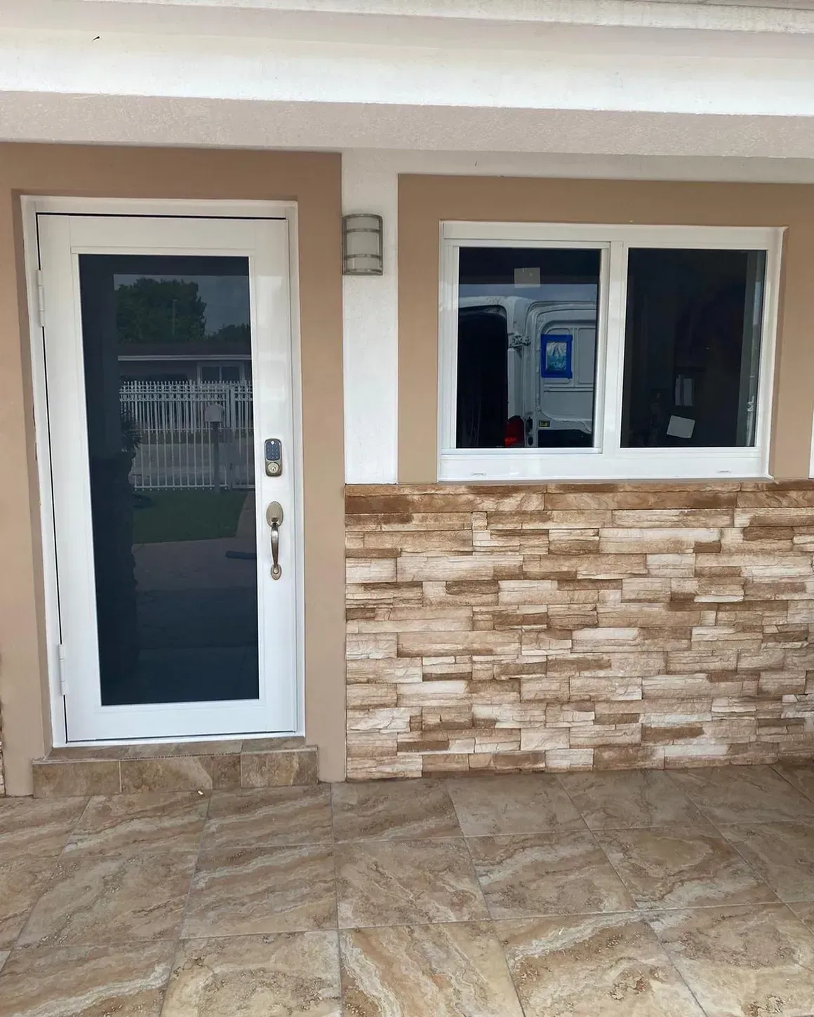 Exterior view of a house entry with a white door, a window, and stone accent wall.