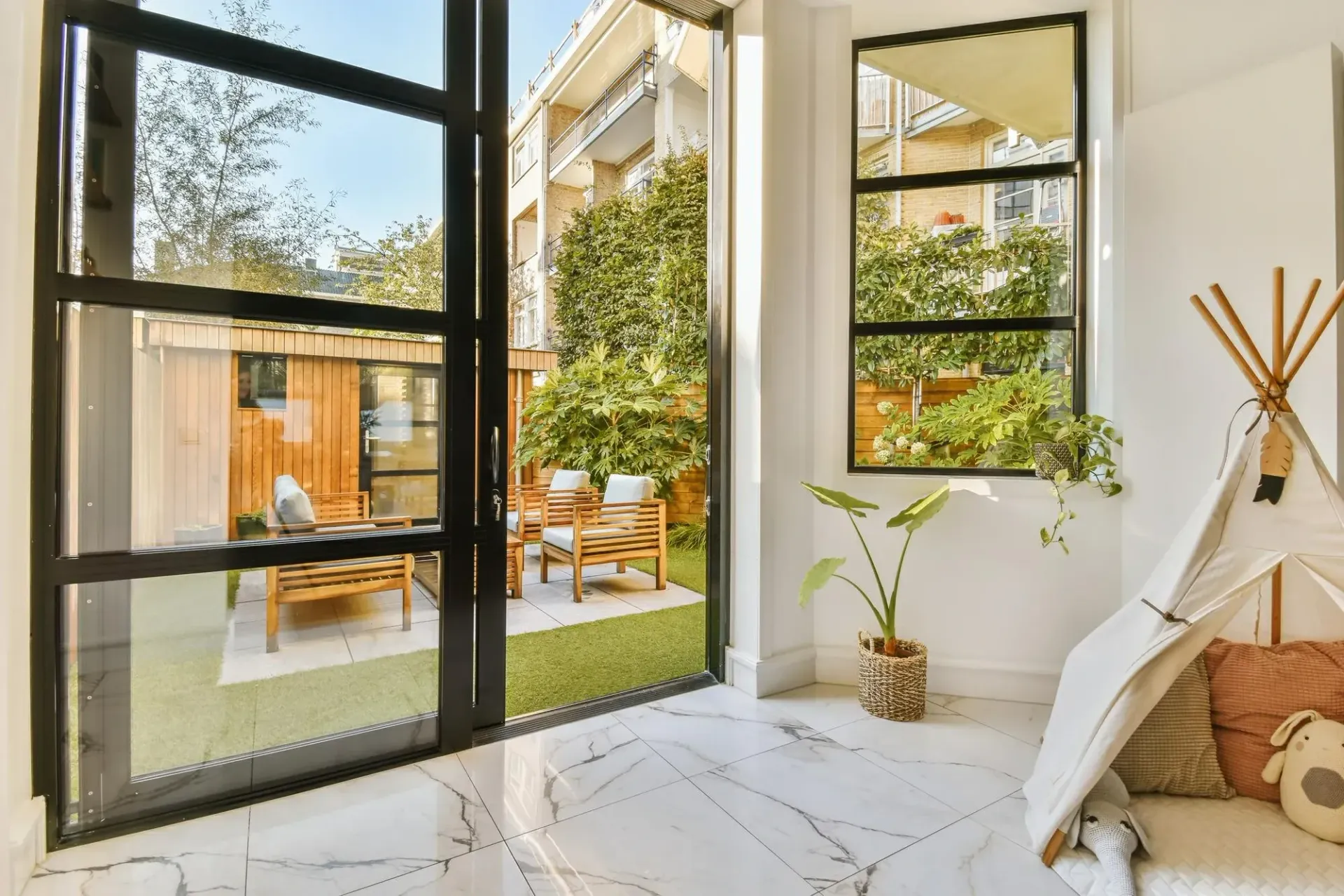 Open glass door and window with black frames, showcasing a backyard patio and a play area with a teepee.
