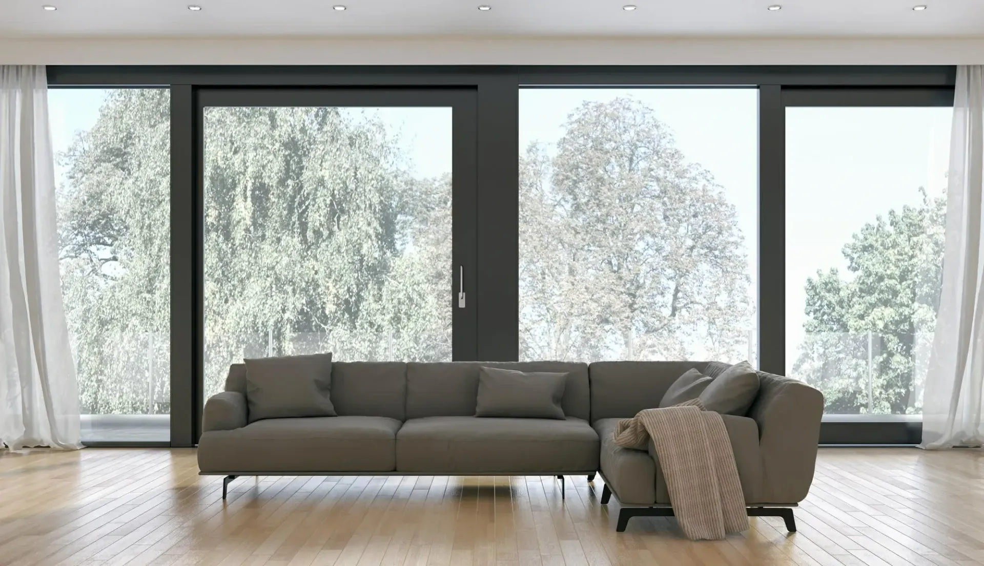 Sala de estar moderna con sofá seccional marrón, ventanas grandes y cortinas blancas transparentes.