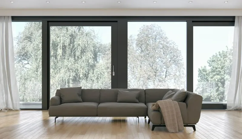 Gray sectional sofa in a bright room with large windows overlooking trees.