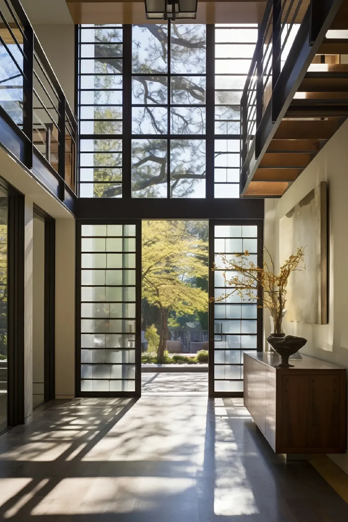 Vista interior de una casa moderna con grandes ventanales y puerta que da a una soleada vista exterior.