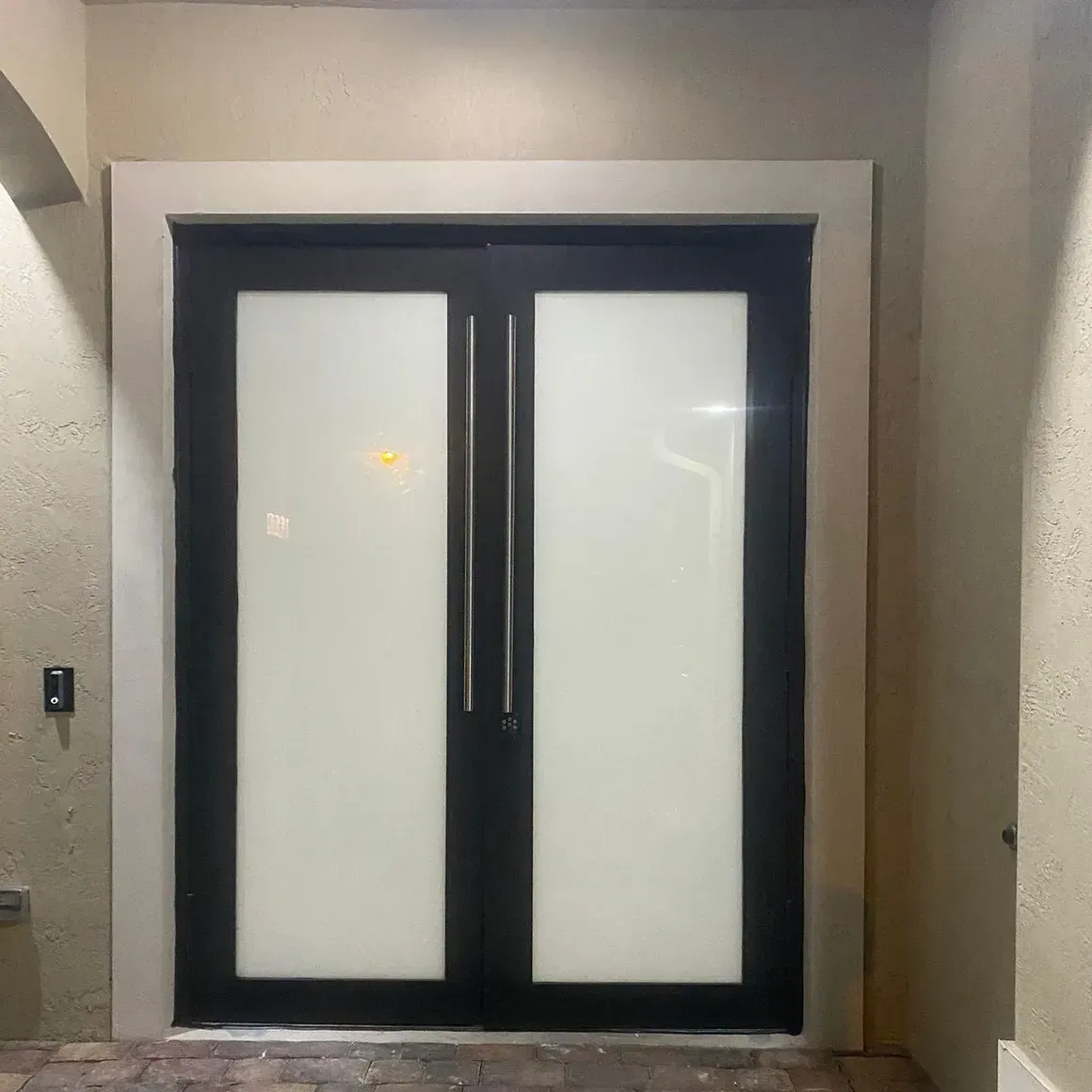 Double black entry doors with frosted glass panels and long silver handles.