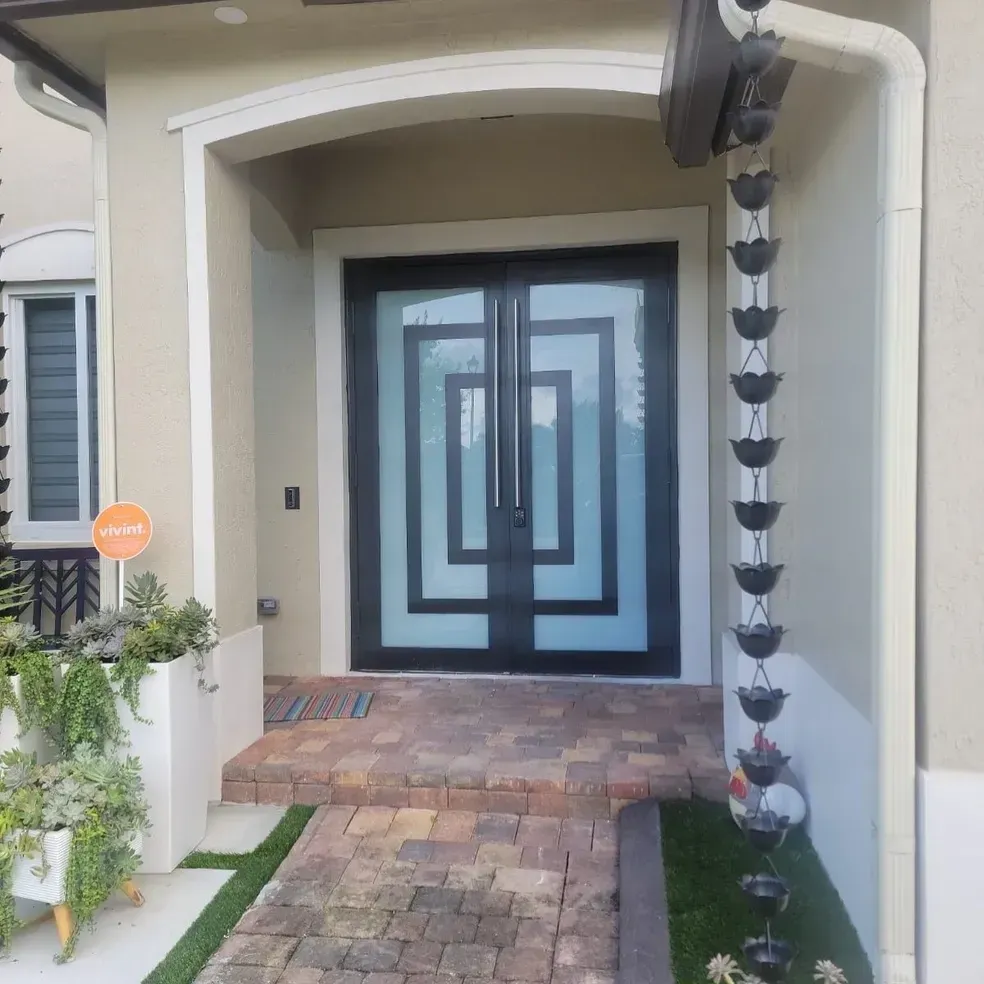 Double black front doors with geometric glass design, under a white arch. Brick pathway.