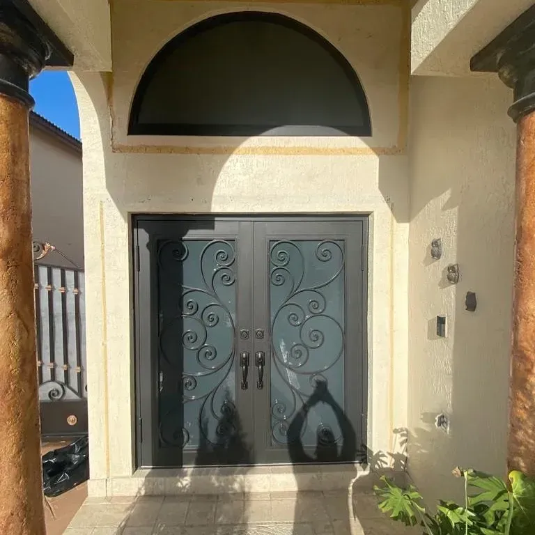 Puertas de entrada dobles negras con volutas y ventana arqueada en la parte superior.