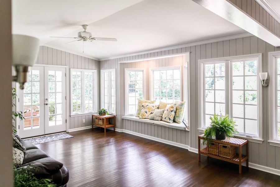 Bright sunroom with white walls, large windows, dark wood floors, and wicker chairs with cushions.