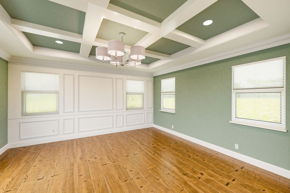 Empty living room with hardwood floors, green coffered ceiling, and white-paneled walls and windows