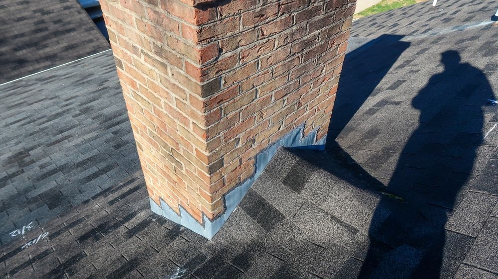 Brick chimney on a shingled roof with a person’s shadow cast beside it.