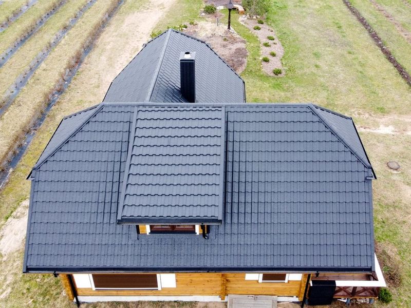 Aerial view of a house with a dark gray roof and dormer, surrounded by grass and paths.